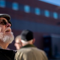 Man with sunglasses and hat on looks up at building